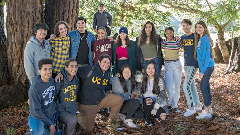 Group of students with their arms around each other next to redwood trees posing for a photo.