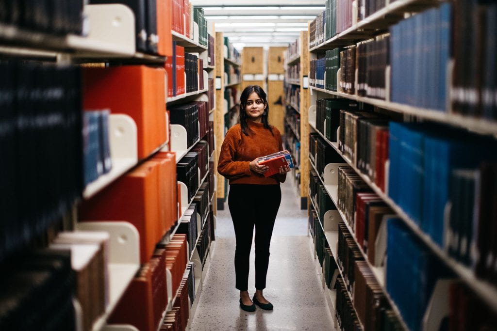 Person standing between rows of books in the library.